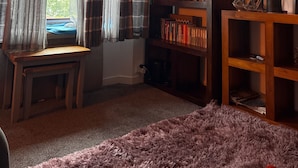 A cozy room with a window, a bookshelf, a small table, and a purple rug. - Apartment Sleeps 2 With Parking (Aberdeen)