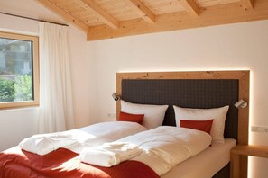Ein Doppelbett mit hölzernem Kopfteil, weißer Bettwäsche und roten Kissen.
