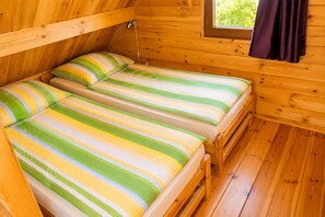 Eine kleine Holzhütte mit zwei Einzelbetten, einem Fenster und einem Vorhang.