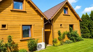 A wooden house with a sloped roof, a small porch, and a visible air conditioning unit. - Cottages for 4 People With a Swimming Pool (Kamien Pomorski)