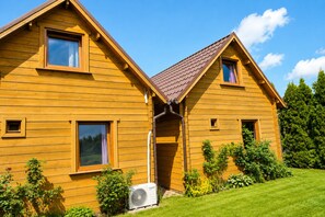 A wooden house with a sloped roof, a small porch, and a visible air conditioning unit. - Cottages for 4 People With a Swimming Pool (Kamien Pomorski)