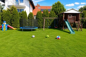 Ein Garten mit Trampolin, Rutsche und Spielhaus.