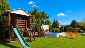 A wooden playhouse with a slide, a small pool, and two lounge chairs in a grassy yard. - Cottages for 4 People With a Swimming Pool (Kamien Pomorski)