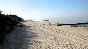 A sandy beach with a wooden pier extending into the water, a clear sky, and sparse vegetation along the shore. - Cottages for 4 People With a Swimming Pool (Kamien Pomorski)