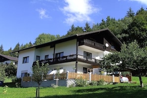 Ein zweistöckiges Gebäude mit Balkon, Carport und kleinem Garten.