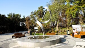 Ein öffentlicher Park mit einer modernen Skulptur, Bänken und Bäumen.