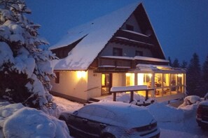 Un edificio cubierto de nieve con un balcón y un interior iluminado, rodeado de nieve.