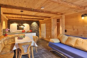 Ein gemütliches Blockhaus-Interieur mit Essbereich, Kamin aus Stein und einem blauen Sofa.