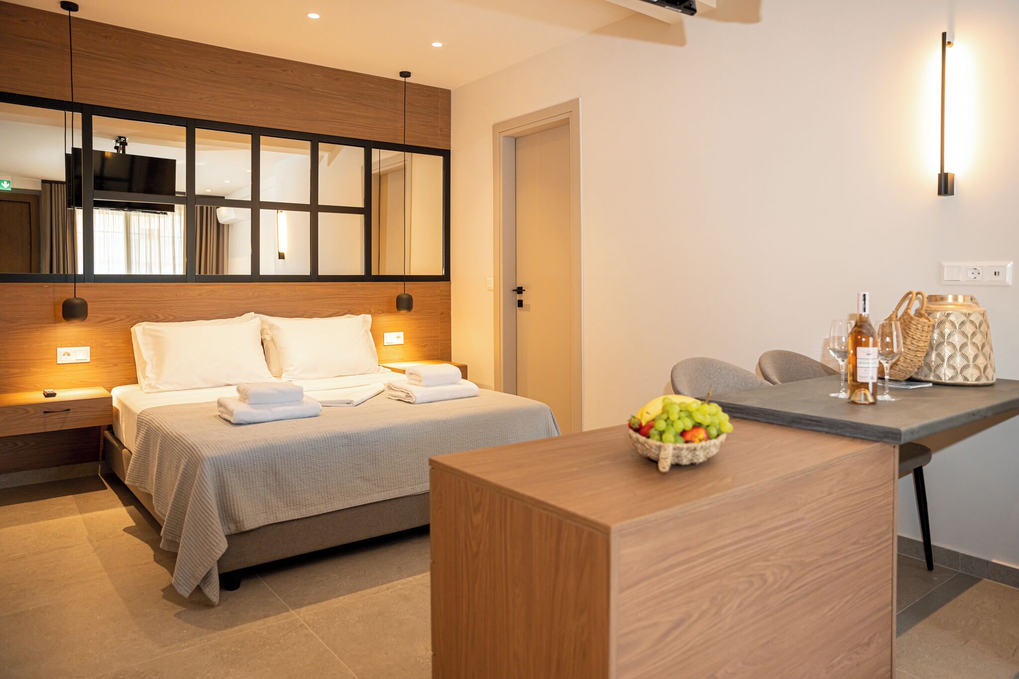Une chambre d’hôtel moderne avec un lit, une table de chevet et un panier de fruits posé sur un bureau en bois.