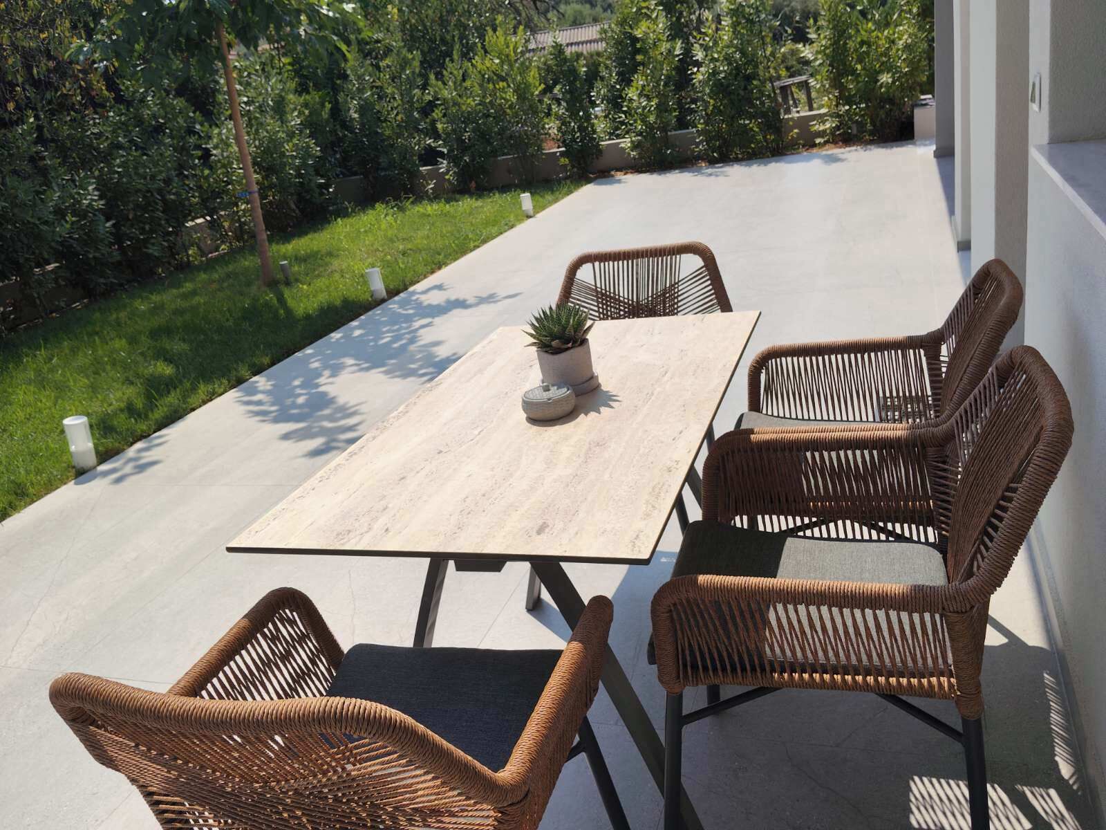 Un patio al aire libre con una mesa rectangular y cuatro sillas de mimbre.
