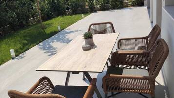 Un patio al aire libre con una mesa rectangular y cuatro sillas de mimbre.