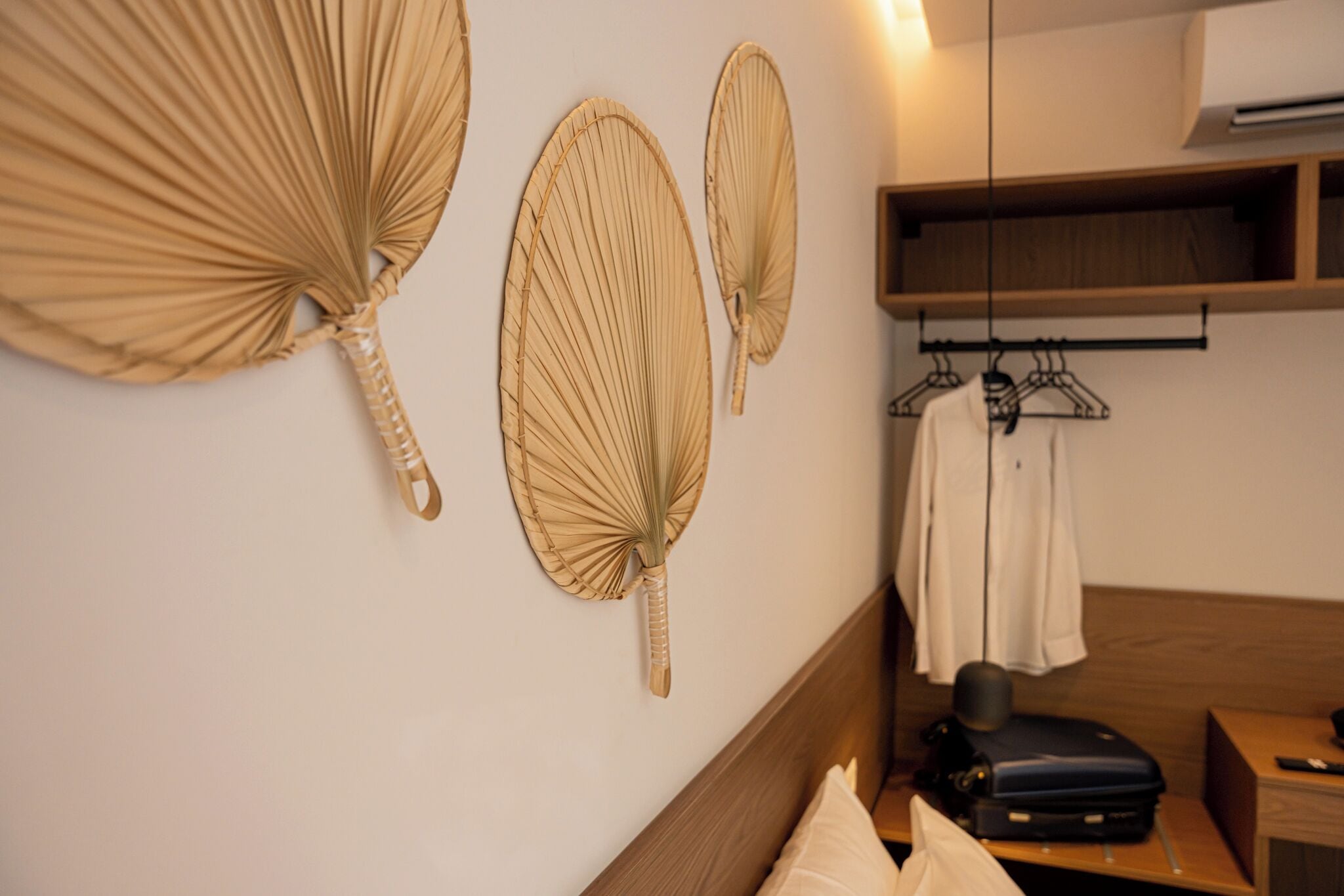 Ein Hotelzimmer mit Bett, Nachttisch, einer Kleiderstange und dekorativen Wandventilatoren.