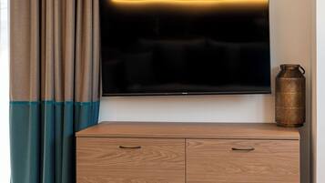 Ein modernes Hotelzimmer mit einem Flachbildfernseher an einem Holzschrank, einem runden Tisch mit weißem Teller und einer dekorativen Metallvase.