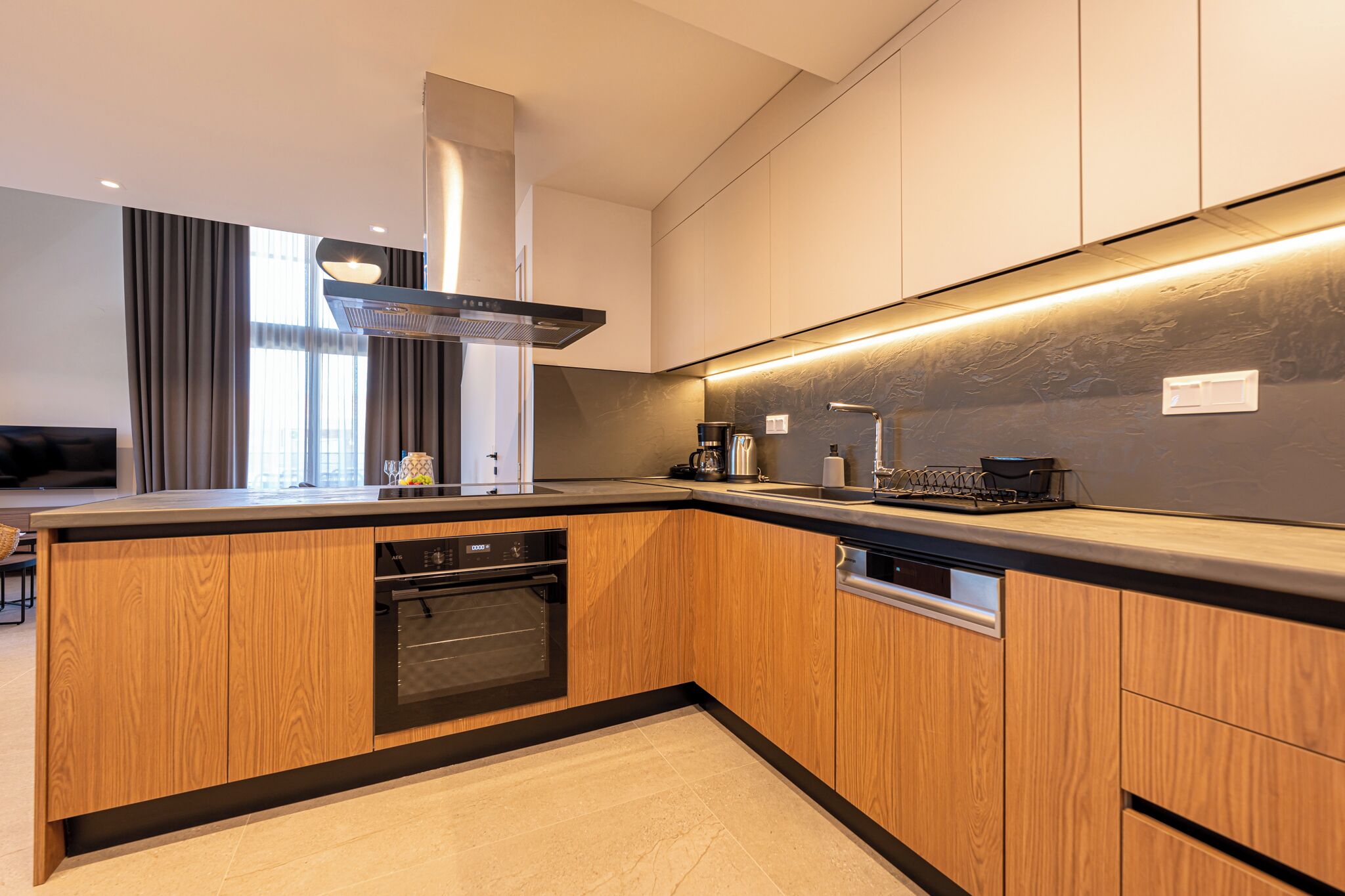 Una cocina moderna con armarios de madera, horno empotrado, extractor de humos y una encimera con cafetera y hervidor.