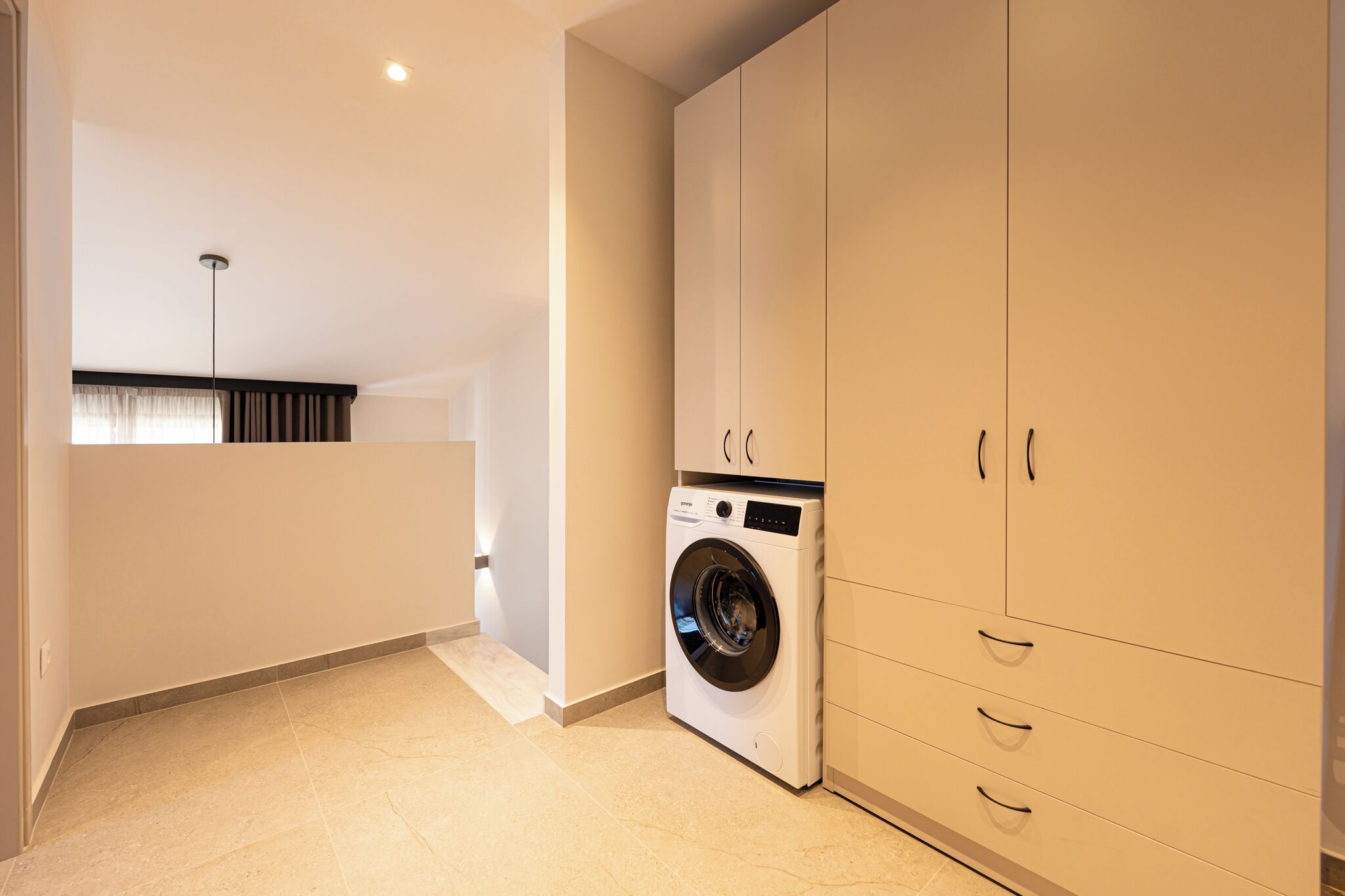 A laundry room with a washing machine, cabinets, and a ceiling light.