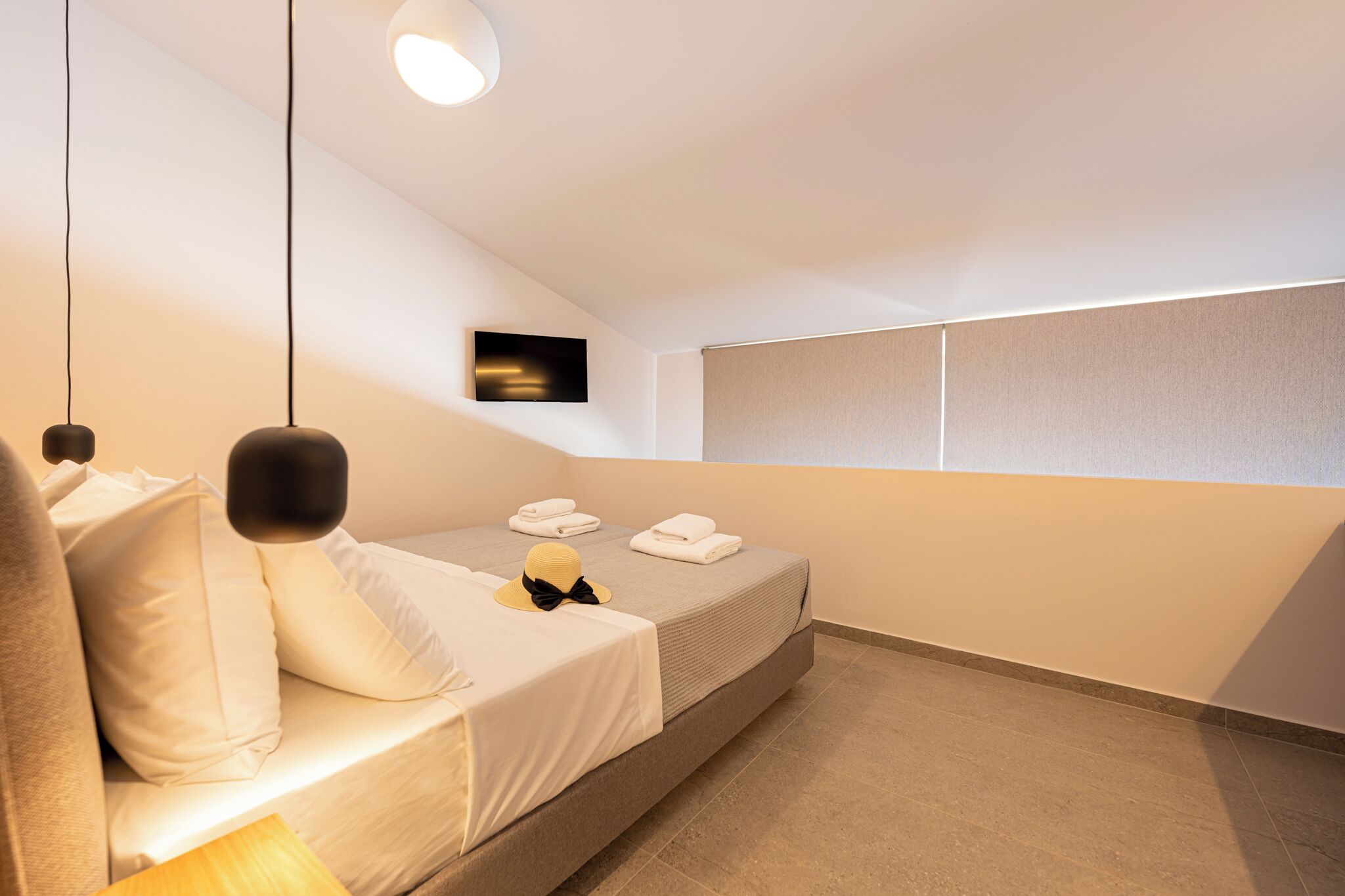 A modern hotel room with a bed, pillows, a hat, and a towel on the bed.