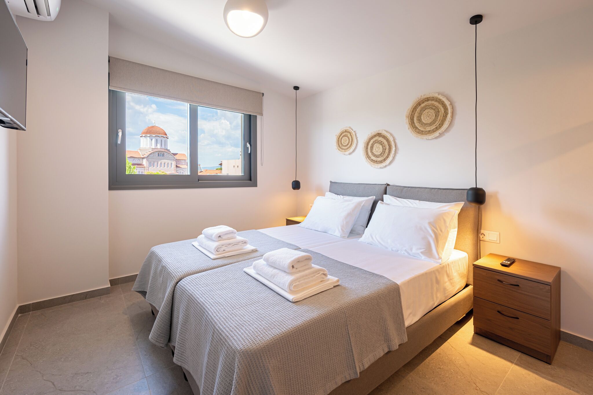 A hotel room with a bed, two bedside tables, a window with a view of a building, and decorative wall art.