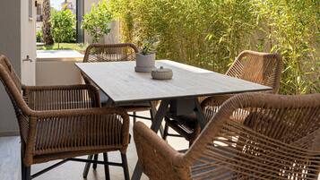 An outdoor patio with a table and wicker chairs, surrounded by greenery.