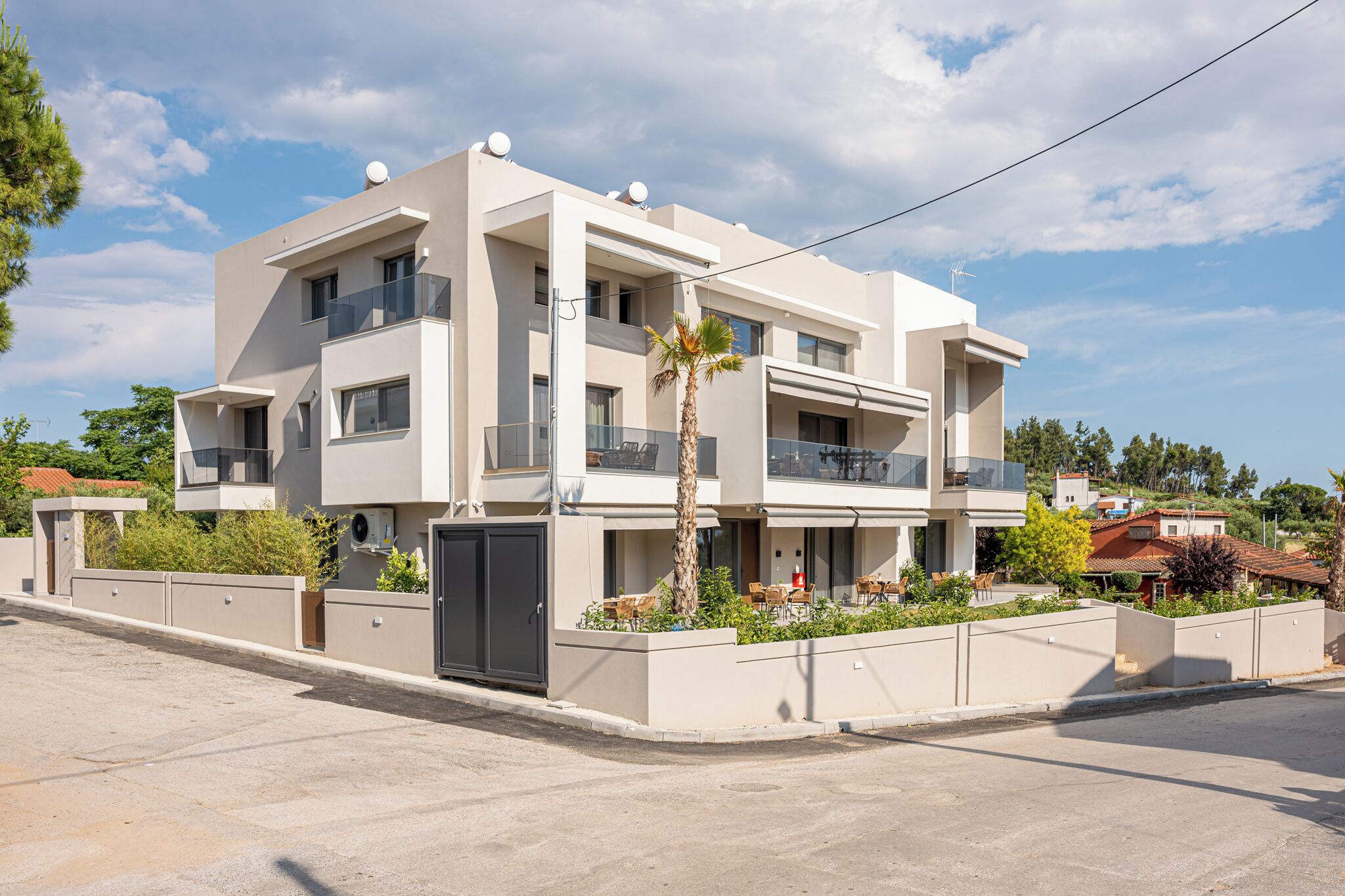 Un moderno edificio residencial de varios pisos con balcones, entrada porticada y un jardín ajardinado.