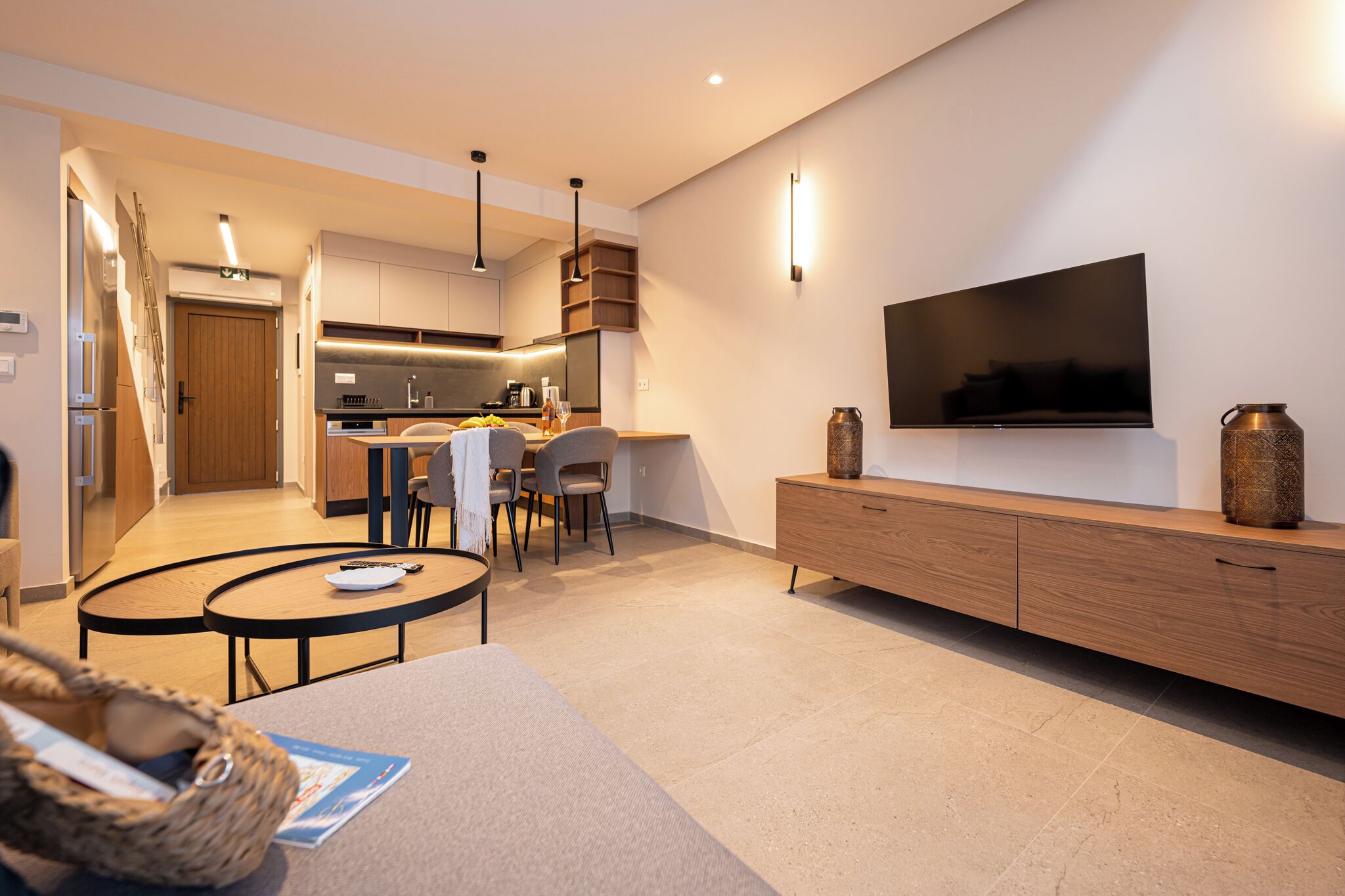 A modern living room with a TV, wooden furniture, and a kitchen in the background.