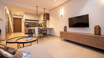 A modern living room with a TV, wooden furniture, and a kitchen in the background.