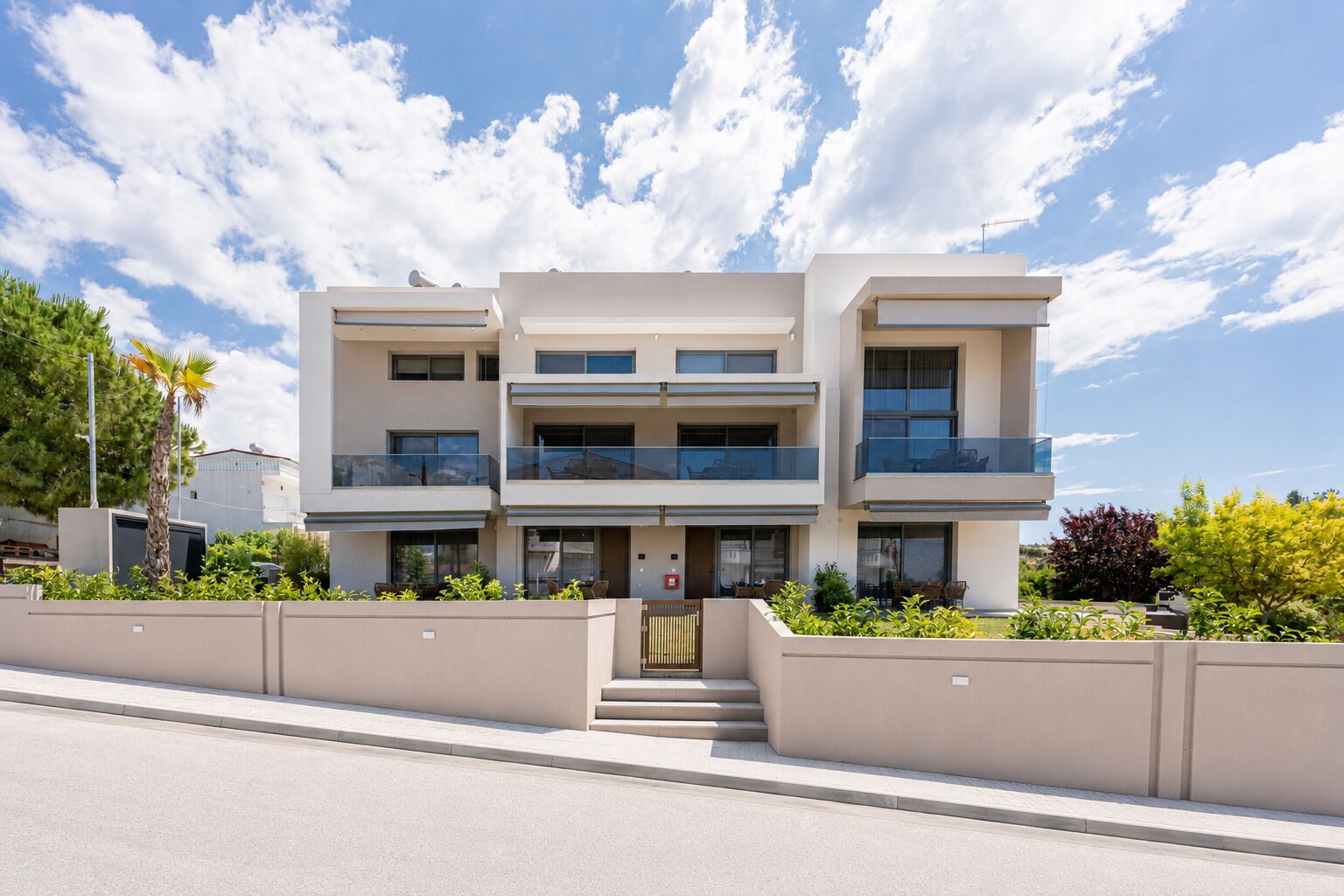 A modern multi-story building with balconies, a gated entrance, and a clear sky.