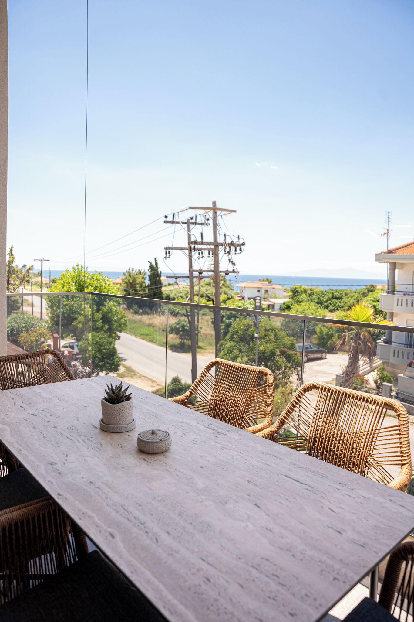 A balcony with wicker chairs, a marble table, and a view of the sea and power lines.