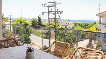 A balcony with wicker chairs, a marble table, and a view of the sea and power lines.