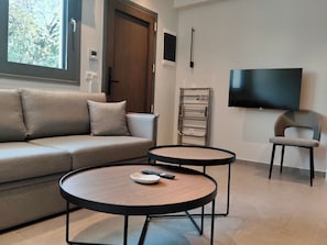 Una sala de estar moderna con un sofá, dos mesas redondas, un televisor y una silla.