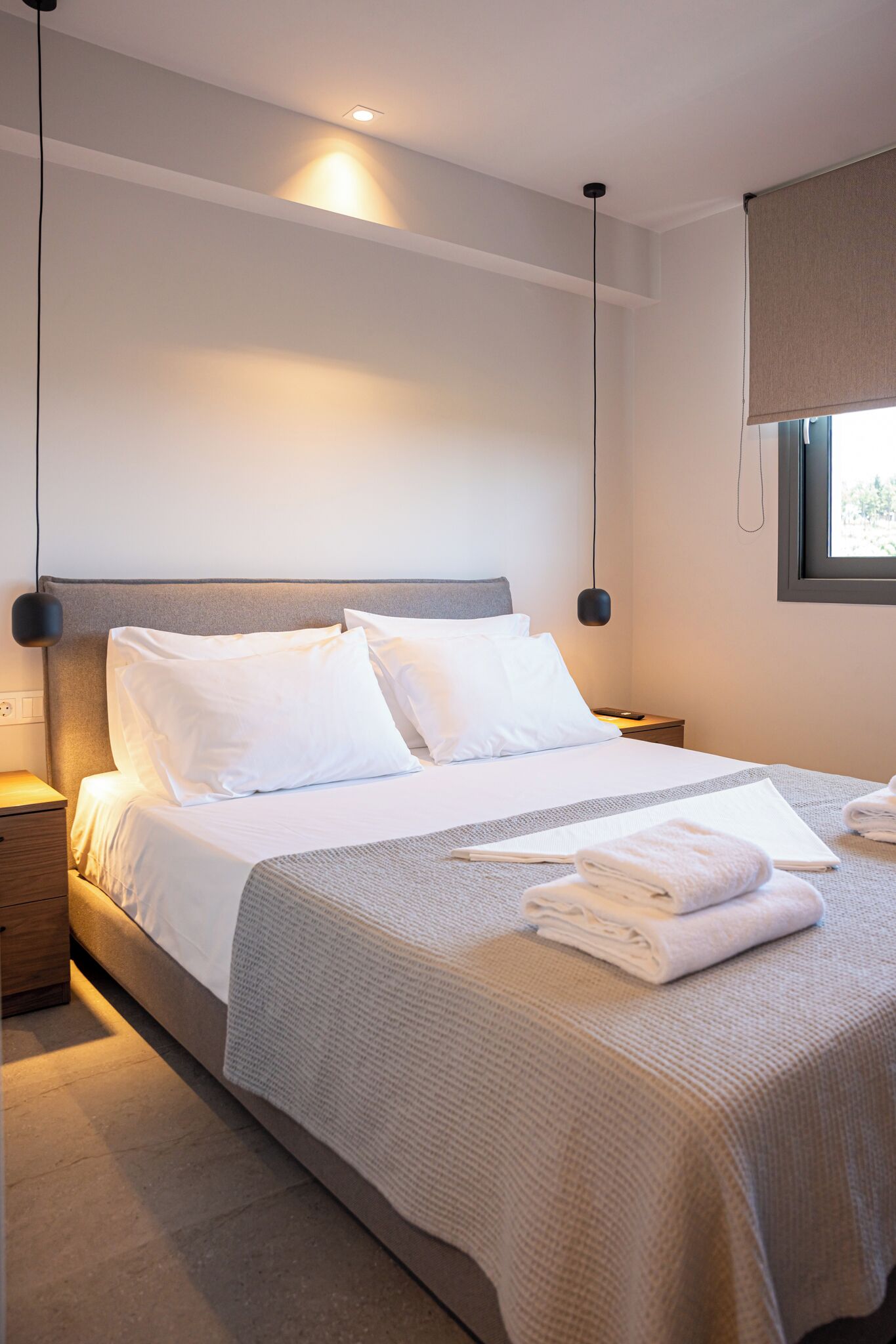 A modern hotel room with a large bed, bedside tables, and a window with a view.