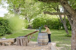 A child operating a water pump in a park with trees and a wooden structure.