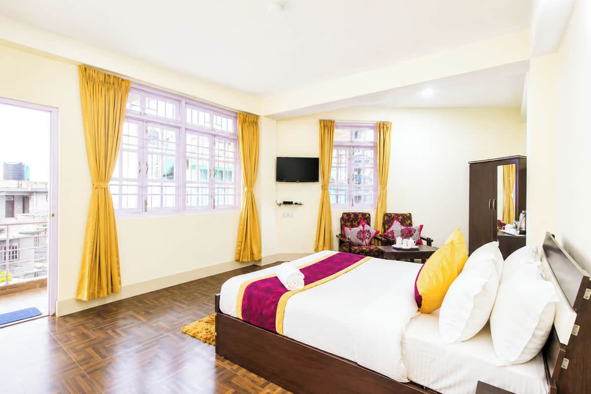 Quarto de hotel com cama, duas janelas com cortinas, televisão de tela plana e vista para o exterior.