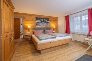 Een slaapkamer met houten lambrisering, een bed, twee bedlampen, een radiator en een raam met rode gordijnen.