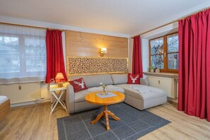 Een gezellige kamer met een houten paneelwand, een ronde houten tafel, een bank en rode gordijnen.