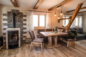 A cozy living room with a stone wall, a fireplace, wooden furniture, and a dining area.