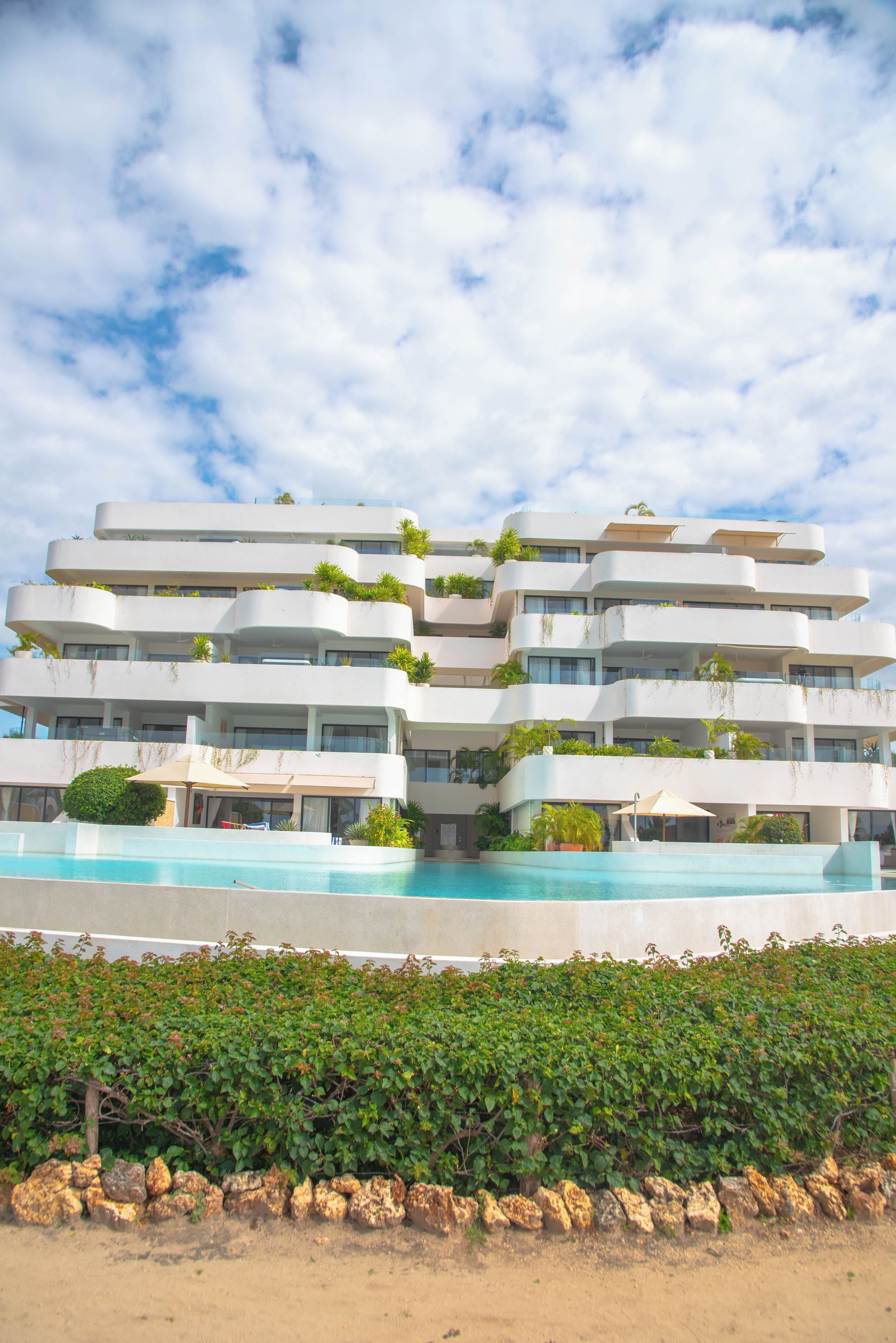 Hotel com vários andares, piscina, varandas com plantas e céu claro.