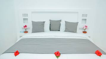 Una cama con un cubrecolcha gris, almohadas blancas y flores rojas.