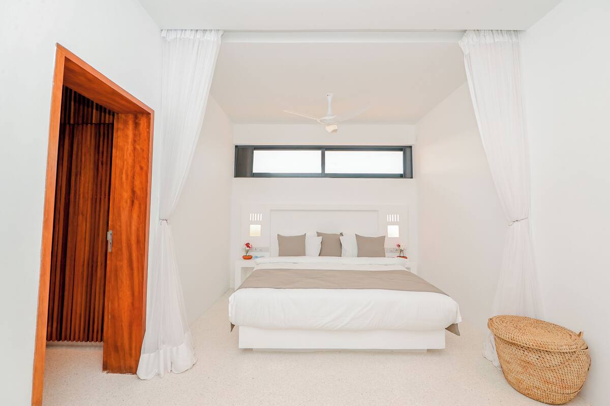 A bedroom with a bed, a ceiling fan, a window, a nightstand, and a woven basket.