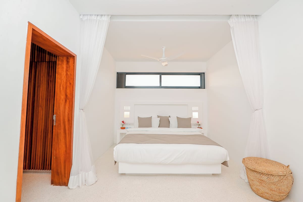 A bedroom with a bed, a ceiling fan, a window, a nightstand, and a woven basket.