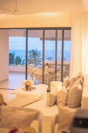 Habitación de hotel moderna con un gran ventanal corredero que da a un balcón con vista al océano y palmeras.