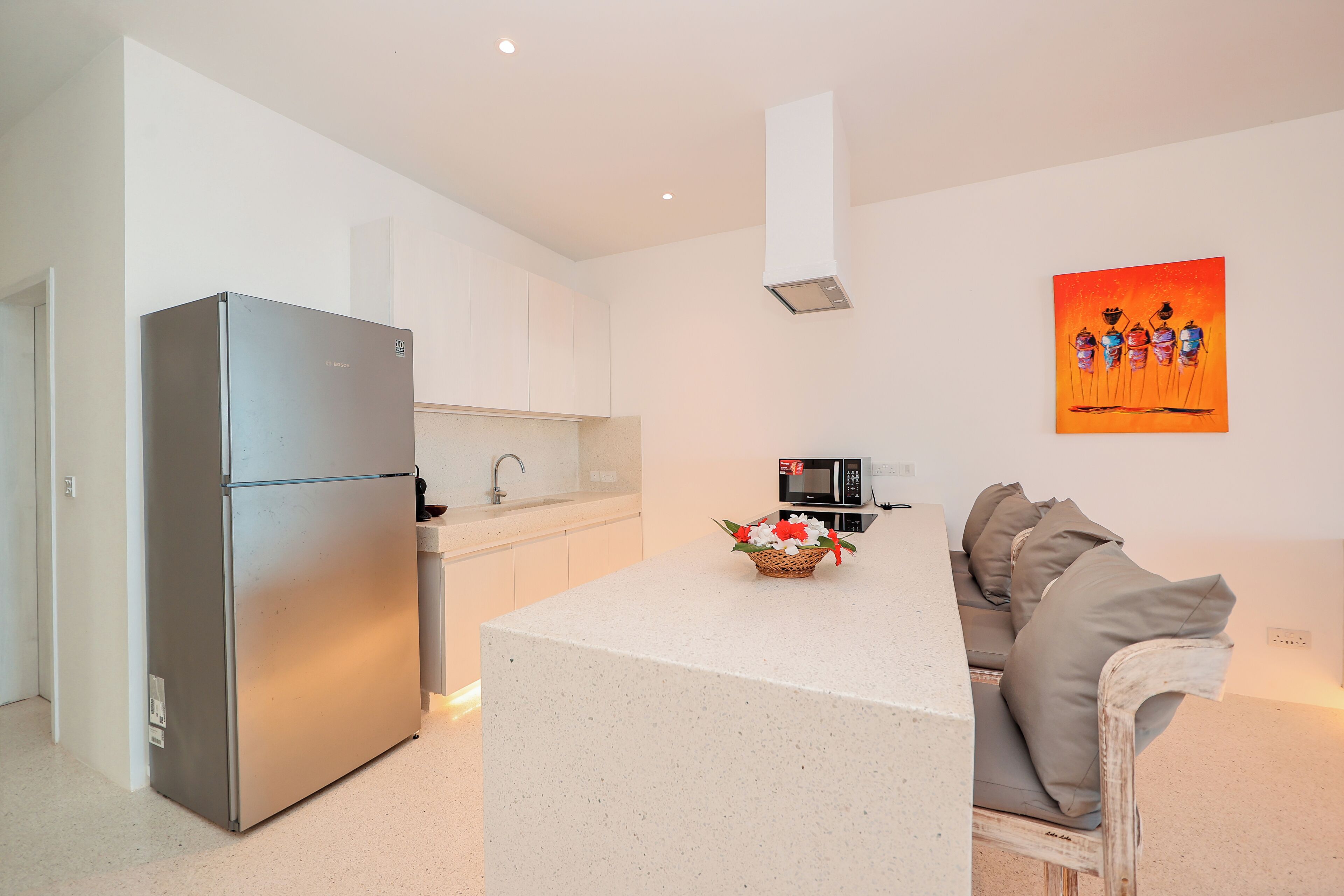 A modern kitchen with a built-in refrigerator, a microwave, and a dining area with a white table and a sofa.
