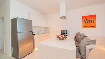 A modern kitchen with a built-in refrigerator, a microwave, and a dining area with a white table and a sofa.