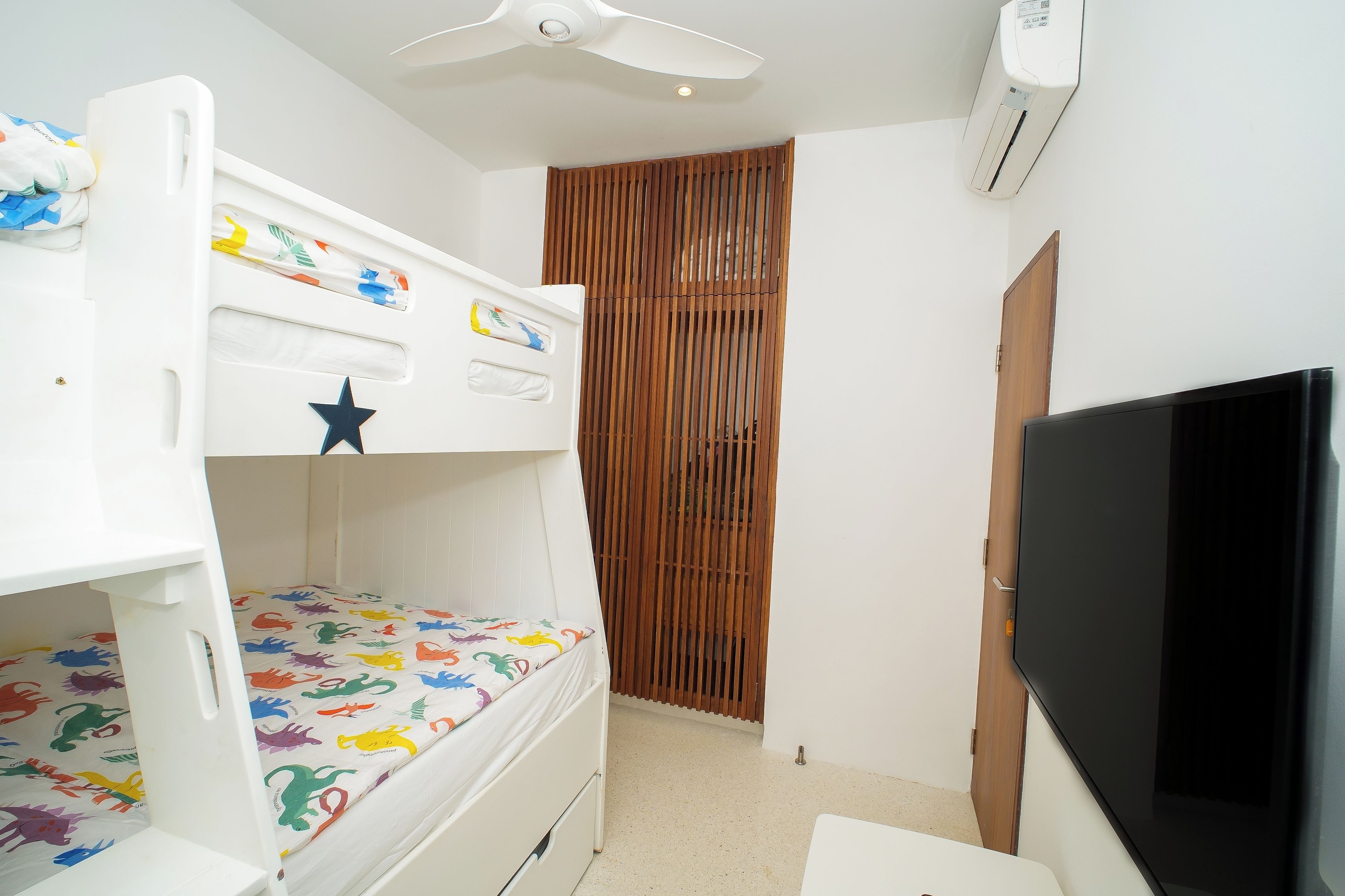 Un lit superposé pour enfant, décoré d’étoiles, avec une télévision et une porte à lattes en bois.