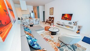 A modern living room with a sofa, a TV, and a dining area in the background. - One Ocean Apartments  by Nest&Nomad (Msambweni)