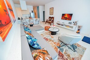 A modern living room with a sofa, a TV, and a dining area in the background. - One Ocean Apartments  by Nest&Nomad (Msambweni)