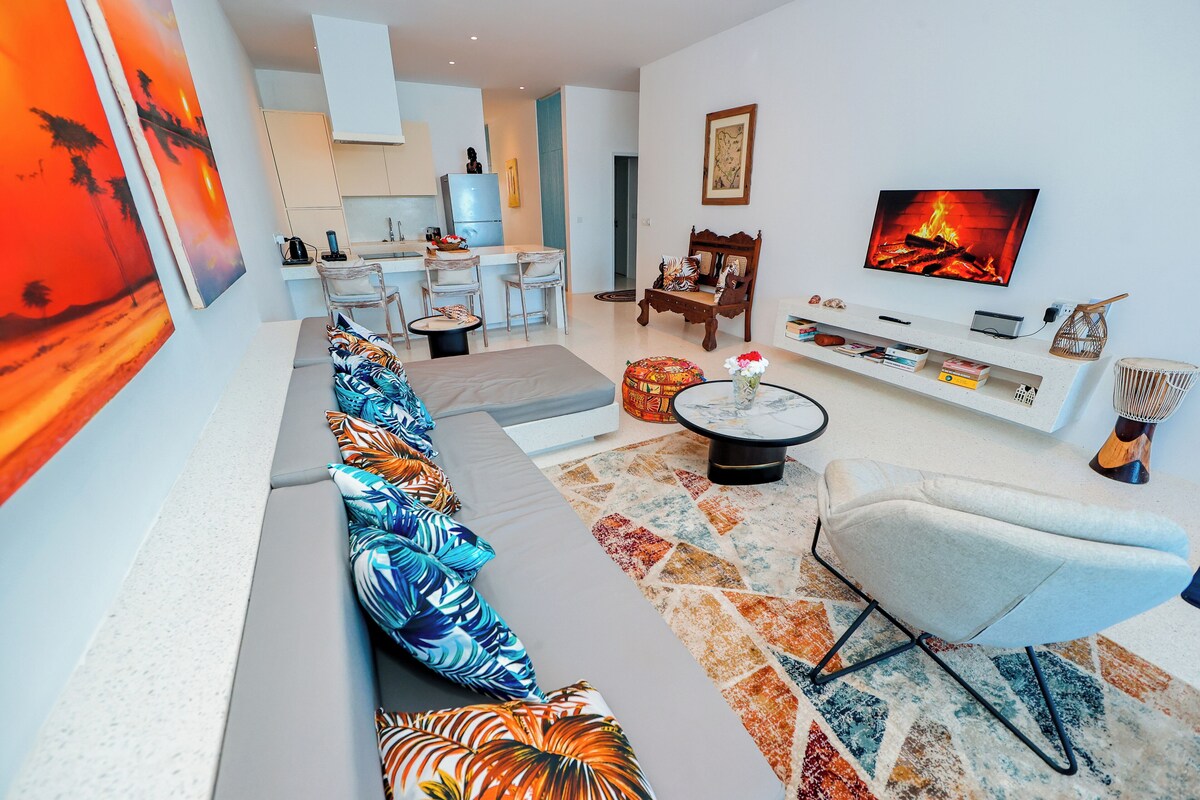 Una sala de estar moderna con sofá, televisor y comedor con sillas y mesa.