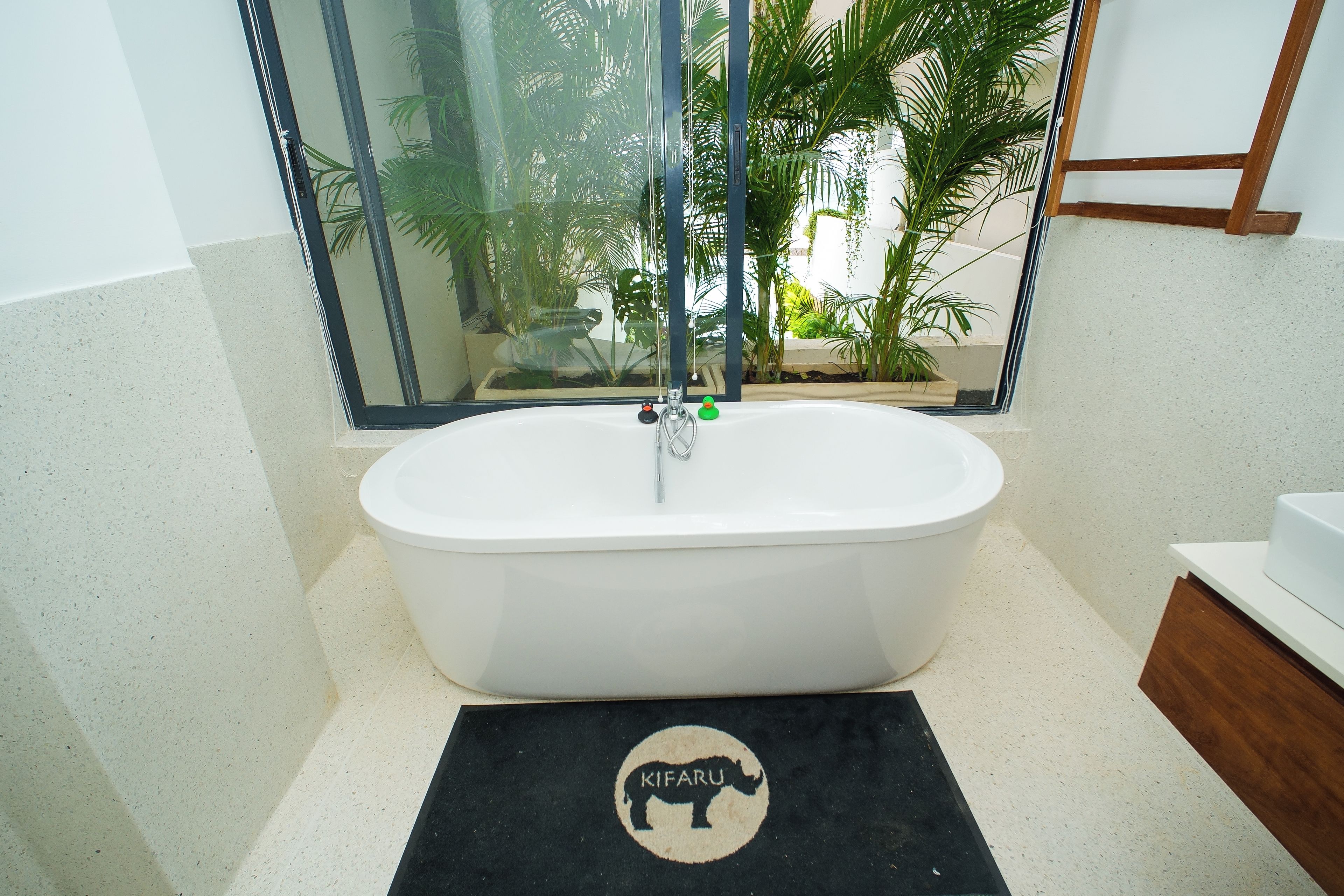 A bathroom with a freestanding bathtub, a glass shower enclosure, and a black mat with a giraffe logo.