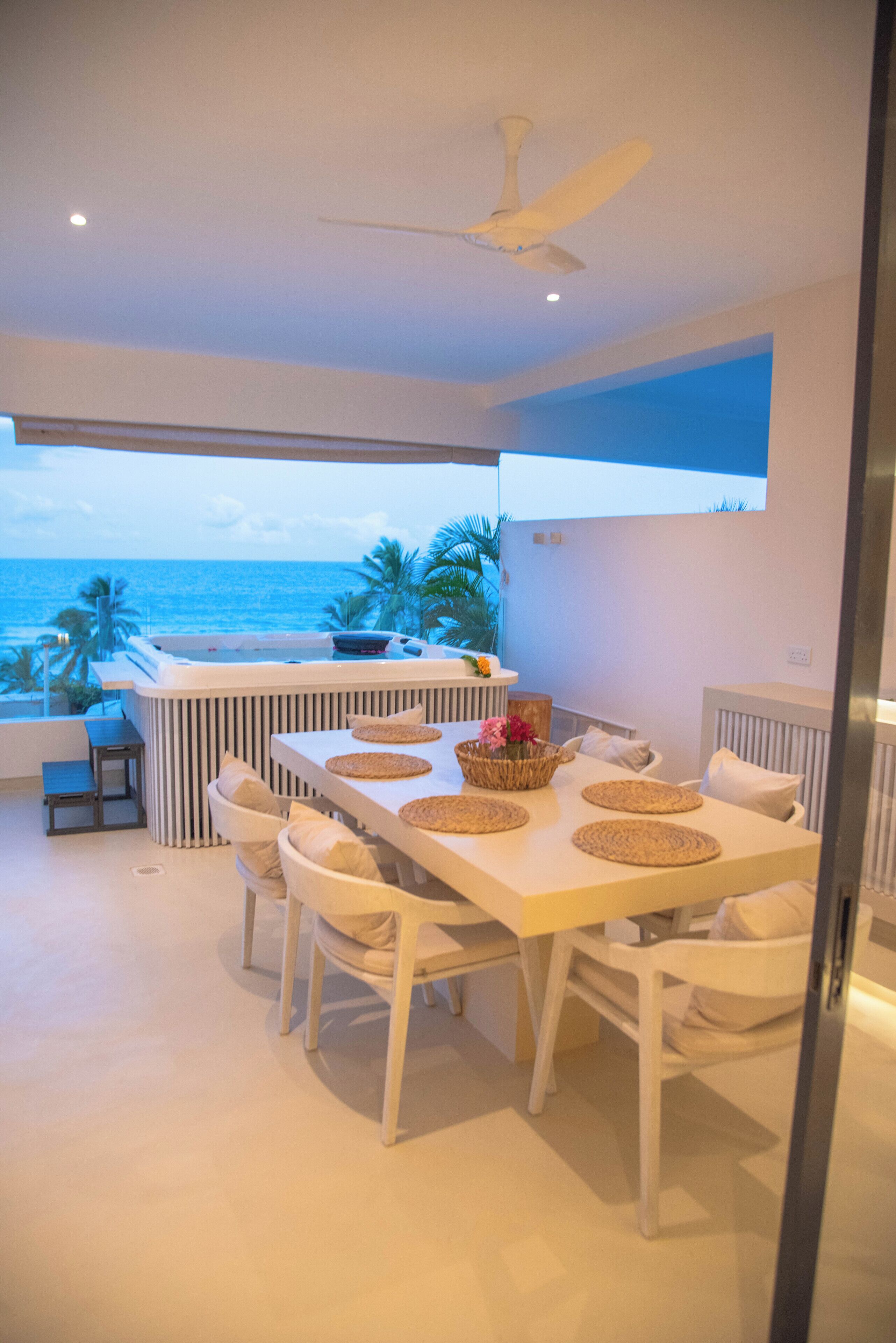 Zona pranzo con tavolo e sedie, una ventola a soffitto e vista sull'oceano.