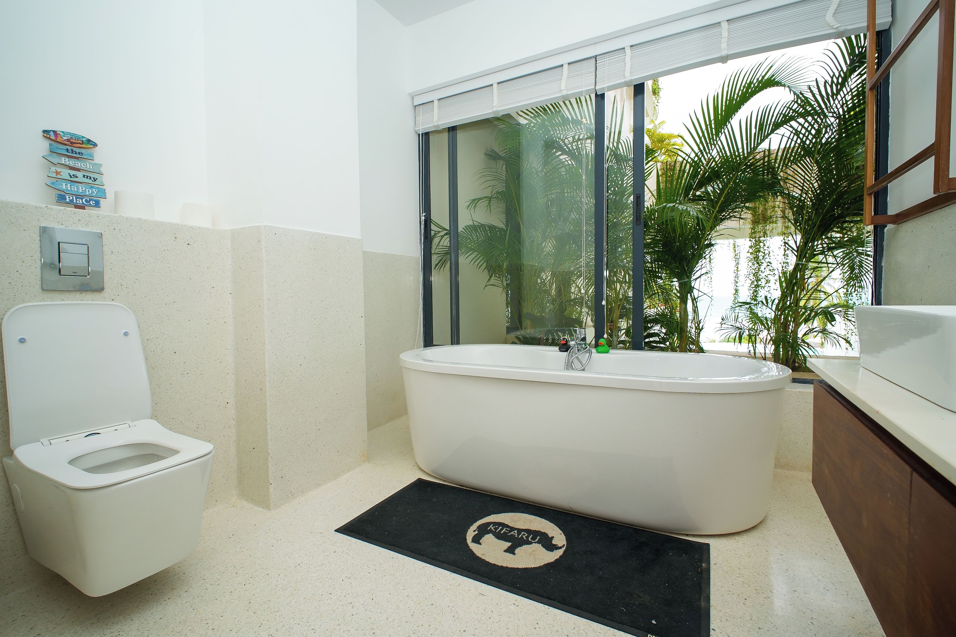 A bathroom with a toilet, a bathtub, and a window with a view of palm trees.