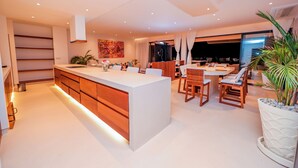A modern kitchen with a central island, wooden cabinets, and a dining area with chairs and a table. - One Ocean Apartments  by Nest&Nomad (Msambweni)